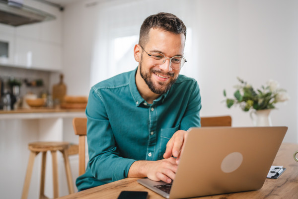 A man sitting at a dining room table working on his laptop