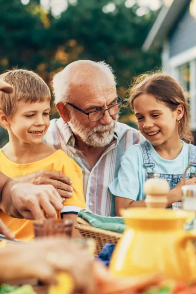 A grandfather shares a meal with two young children, smiling and enjoying their time together at a table.