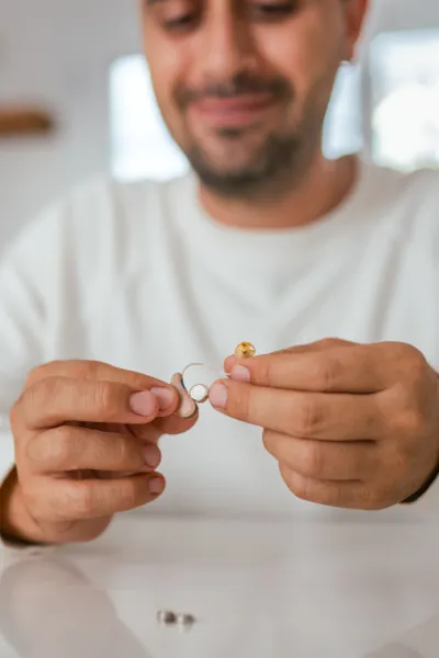 A person holding two small metal components of a hearing aid while looking at them attentively.